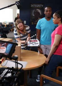 Woman holds a movie slate in front of two actors.